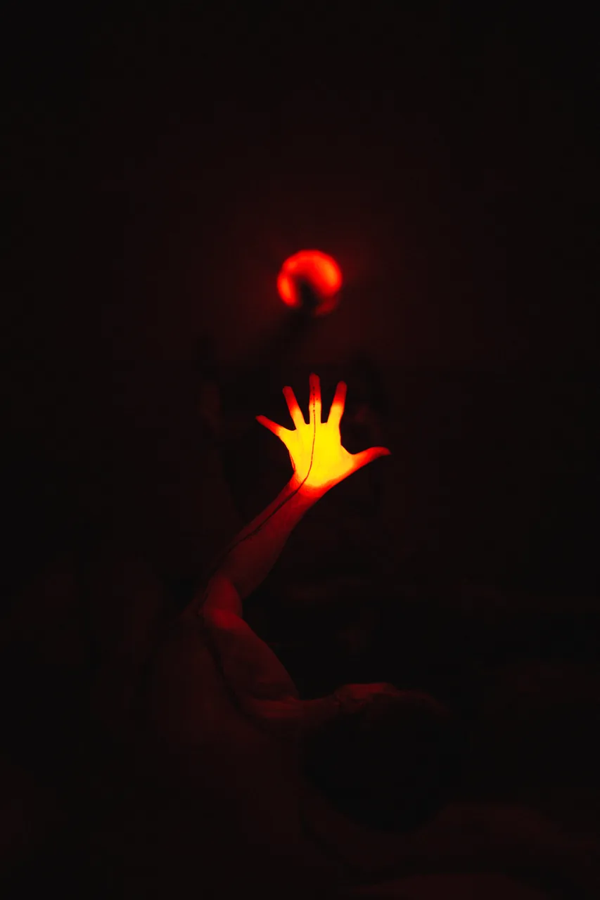 Mano iluminada en amarillo frente a un intérprete en penumbra roja — Abisal